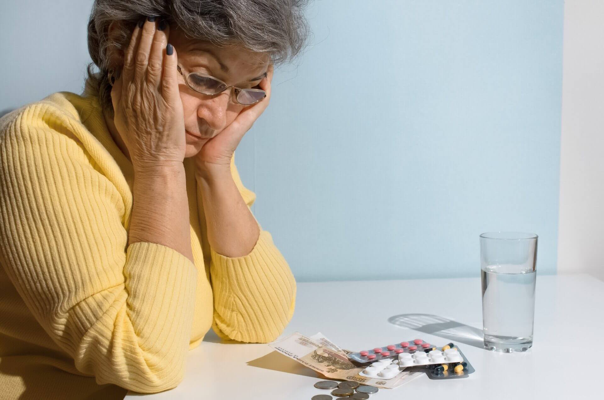 Elderly woman with glasses looking at money and pills on the table